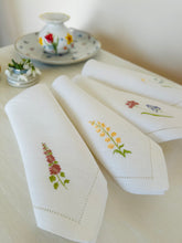 Ielādēt attēlu galerijas skatītājā, white linen napkins with machine‑embroidered meadow wildflowers motifs and hemstitched edges