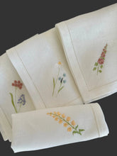 Ielādēt attēlu galerijas skatītājā, white linen napkins with machine‑embroidered meadow wildflowers motifs and hemstitched edges