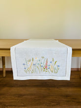 Ielādēt attēlu galerijas skatītājā, white linen table runner with machine‑embroidered meadow wildflowers motifs and hemstitched edges