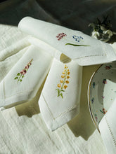 Ielādēt attēlu galerijas skatītājā, white linen napkins with machine‑embroidered meadow wildflowers motifs and hemstitched edges