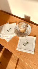 Load image into Gallery viewer, Bring quiet, botanical elegance to your table with these linen coasters embroidered with lily of the valley. Made from natural European linen, they protect surfaces beautifully while adding a refined spring-floral detail. Perfect for coffee moments, hosting, and thoughtful gifting.