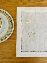 Ielādēt attēlu galerijas skatītājā, white linen placemats with machine‑embroidered meadow wildflowers motifs and hemstitched edges - perfect eco table linens for botanical dining; hostess gifts.