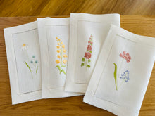Ielādēt attēlu galerijas skatītājā, white linen placemats with machine‑embroidered meadow wildflowers motifs and hemstitched edges - perfect eco table linens for botanical dining; hostess gifts.