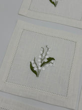 Load image into Gallery viewer, Bring quiet, botanical elegance to your table with these linen coasters embroidered with lily of the valley. Made from natural European linen, they protect surfaces beautifully while adding a refined spring-floral detail. Perfect for coffee moments, hosting, and thoughtful gifting.