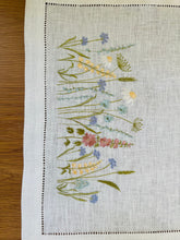 Ielādēt attēlu galerijas skatītājā, white linen table runner with machine‑embroidered meadow wildflowers motifs and hemstitched edges