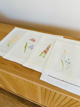 Ielādēt attēlu galerijas skatītājā, white linen placemats with machine‑embroidered meadow wildflowers motifs and hemstitched edges - perfect eco table linens for botanical dining; hostess gifts.