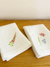 Ielādēt attēlu galerijas skatītājā, white linen napkins with machine‑embroidered meadow wildflowers motifs and hemstitched edges
