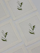 Load image into Gallery viewer, Bring quiet, botanical elegance to your table with these linen coasters embroidered with lily of the valley. Made from natural European linen, they protect surfaces beautifully while adding a refined spring-floral detail. Perfect for coffee moments, hosting, and thoughtful gifting.
