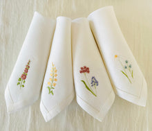 Ielādēt attēlu galerijas skatītājā, white linen napkins with machine‑embroidered meadow wildflowers motifs and hemstitched edges
