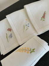 Ielādēt attēlu galerijas skatītājā, white linen napkins with machine‑embroidered meadow wildflowers motifs and hemstitched edges
