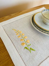 Ielādēt attēlu galerijas skatītājā, white linen placemat with machine‑embroidered meadow wildflowers motifs and hemstitched edges - perfect eco table linens for botanical dining; hostess gifts.
