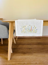 Ielādēt attēlu galerijas skatītājā, white linen table runner with machine‑embroidered meadow wildflowers motifs and hemstitched edges
