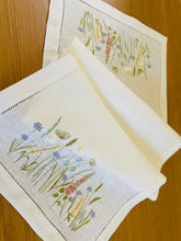 Ielādēt attēlu galerijas skatītājā, white linen table runner with machine‑embroidered meadow wildflowers motifs and hemstitched edges
