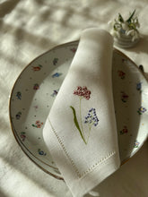 Ielādēt attēlu galerijas skatītājā, white linen napkin with machine‑embroidered meadow wildflowers motifs and hemstitched edges
