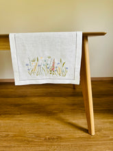 Ielādēt attēlu galerijas skatītājā, white linen table runner with machine‑embroidered meadow wildflowers motifs and hemstitched edges
