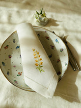 Ielādēt attēlu galerijas skatītājā, white linen napkin with machine‑embroidered meadow wildflowers motifs and hemstitched edges
